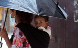 A photo of a woman holding an umbrella and carrying a baby in a sling on her back. The photo was taken in Nepal, which is one of many countries at risk of typhoid related to climate change and extreme weather.