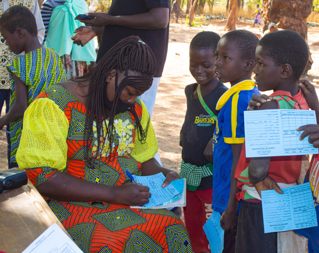 A photo showing a woman filling out a typhoid vaccine card while three young children smile and watch nearby.